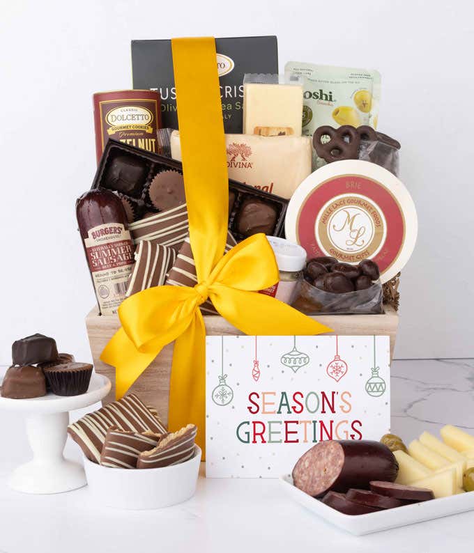 A wooden basket filled with chocolates, summer sausage, cheeses, crackers, crisps, mustard, and snacks, with displays of chocolate treats, sliced sausage, olives, and cheese arranged with a Season's Greetings message.