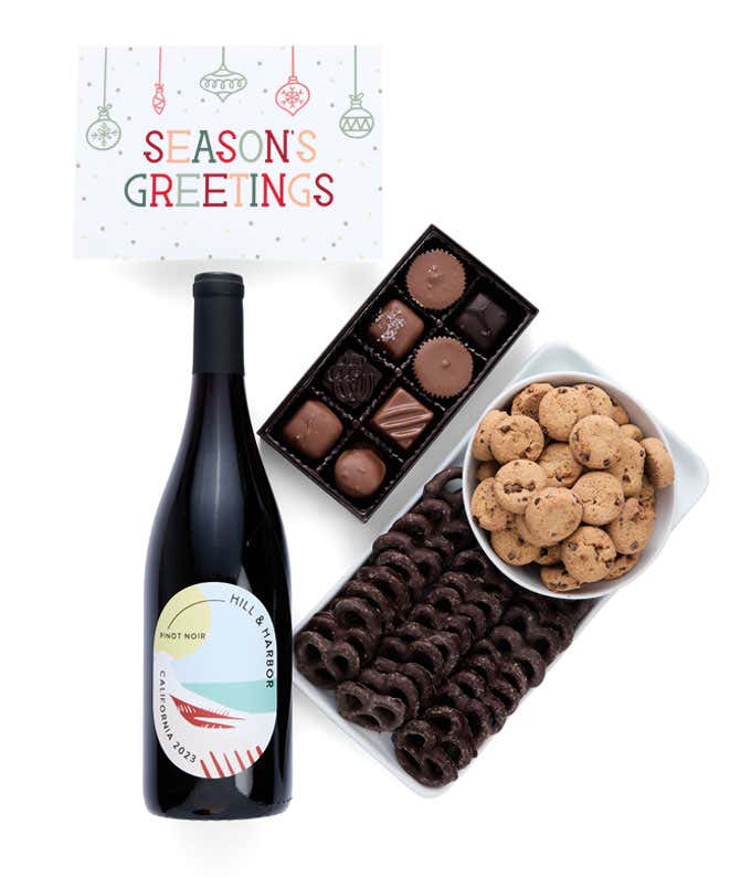 A holiday gift set with abottle of Hill & Harbor Pinot Noir, a box of assorted chocolates, a bag of chocolate-covered pretzels, a box of mini chocolate chip cookies, and a Season's Greetings message card.