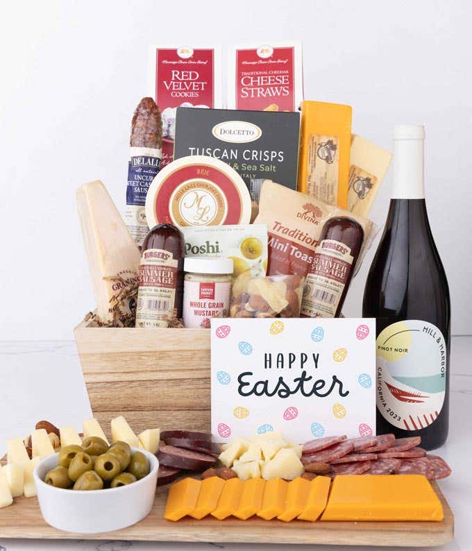 A wooden gift basket filled with summer sausages, 3 cheeses, Tuscan crisps, mini toasts, red velvet cookies, cheese straws, nuts, mustard, and a bottle of wine with an Easter card.