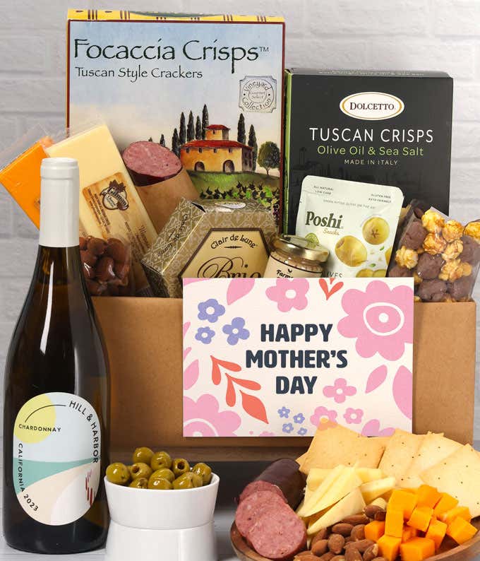 A charcuterie spread with 3 cheeses, summer sausage, olives, crackers, mustard, almonds, and chocolate treats finished with a bottle of Chardonnay and 'Happy Mother's Day' card.