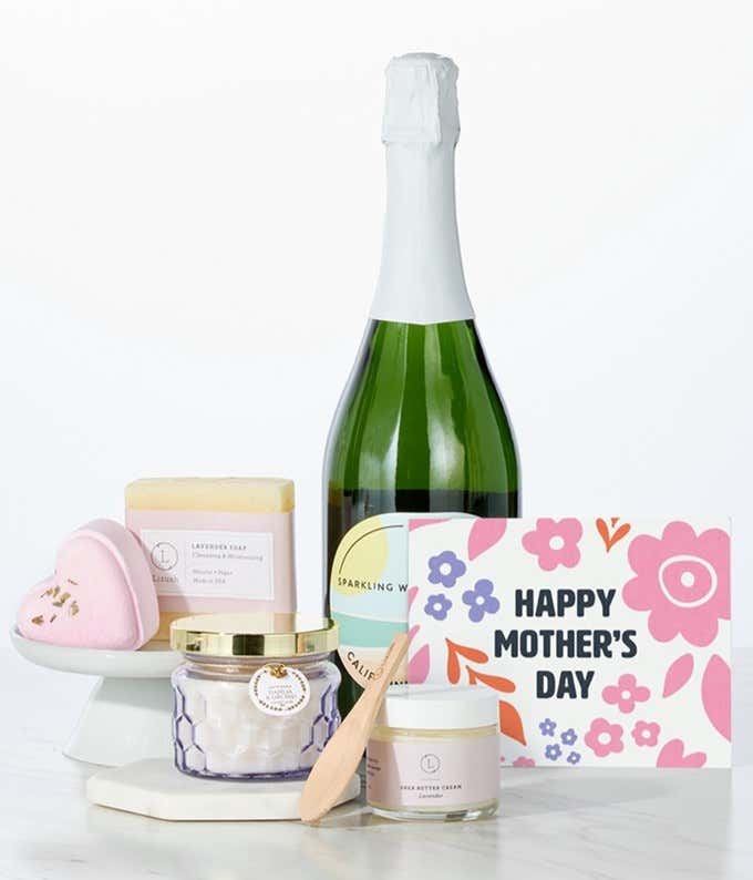 Hill & Harbor California Sparkling Wine paired with spa essentials including artisan lavendar soap, a heart-shaped shower steamer, shea butter cream with wooden scoop, and a candle arranged in a clean display with a Mother's Day card.
