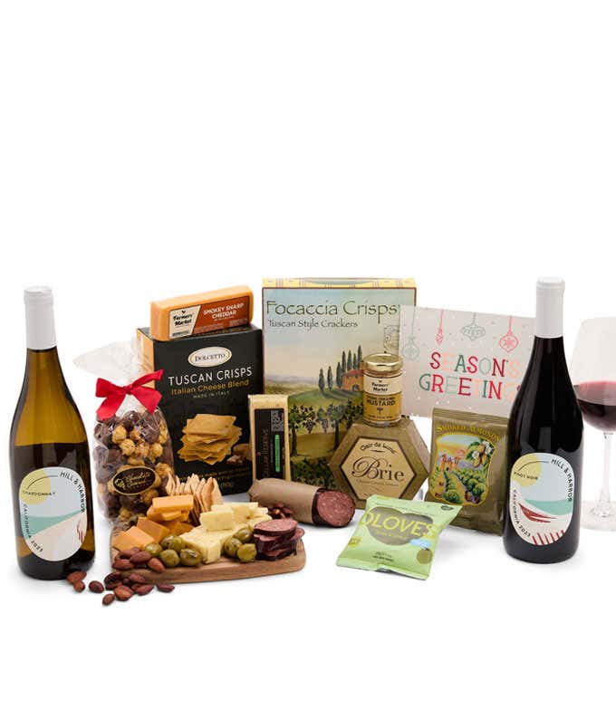 A charcuterie gift set with 3 cheeses, Tuscan crisps, focaccia crackers, olives, mustard, smoked almonds, chocolate-covered popcorn, summer sausage, 2 bottles of wine - red and white, and a Seasons Greetings card.