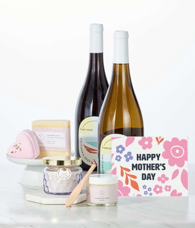 Two bottles of Hill & Harbor California wine paired with spa essentials including artisan lavender soap, a heart-shaped shower steamer, shea butter cream with wooden scoop, and a candle arranged in a clean display with a Mother's Day card.
