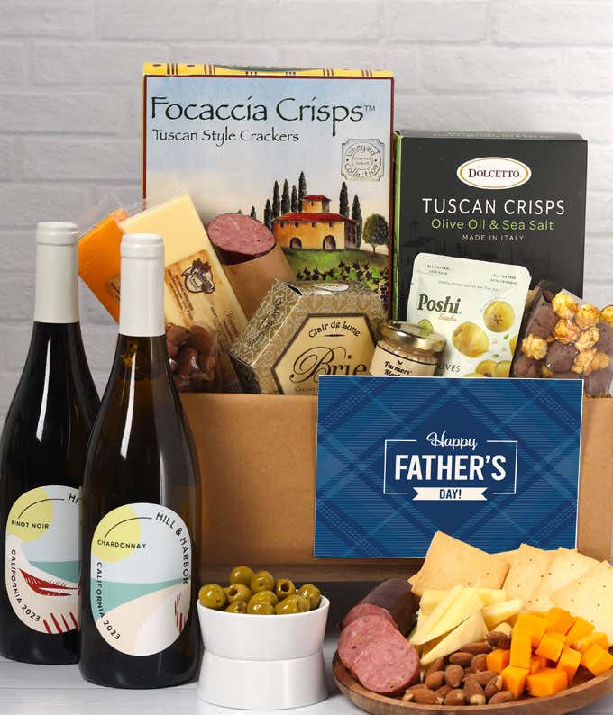 Two bottles of wine with gourmet charcuterie including Tuscan crisps, focaccia crackers, brie, mustard, sausage, 3 cheeses, olives, smoked almonds, and chocolate-covered treats, complete with a 'Happy Father's Day' card.