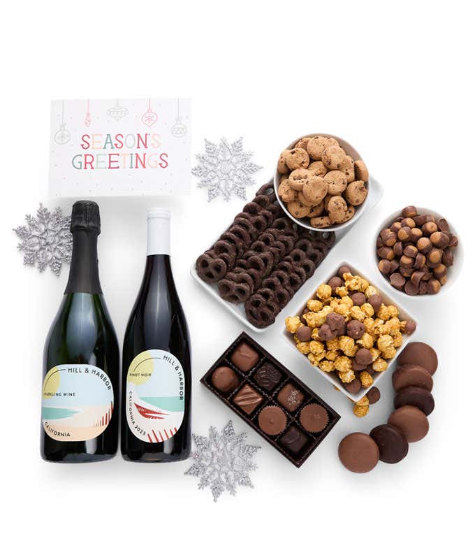 A gift set with bottles of wine - red and sparkling, paired with chocolate pretzels, caramel popcorn, mini cookies, chocolate peanut butter buckeyes, six chocolate-covered Oreos, assorted chocolates, and a festive Seasons Greetings card.