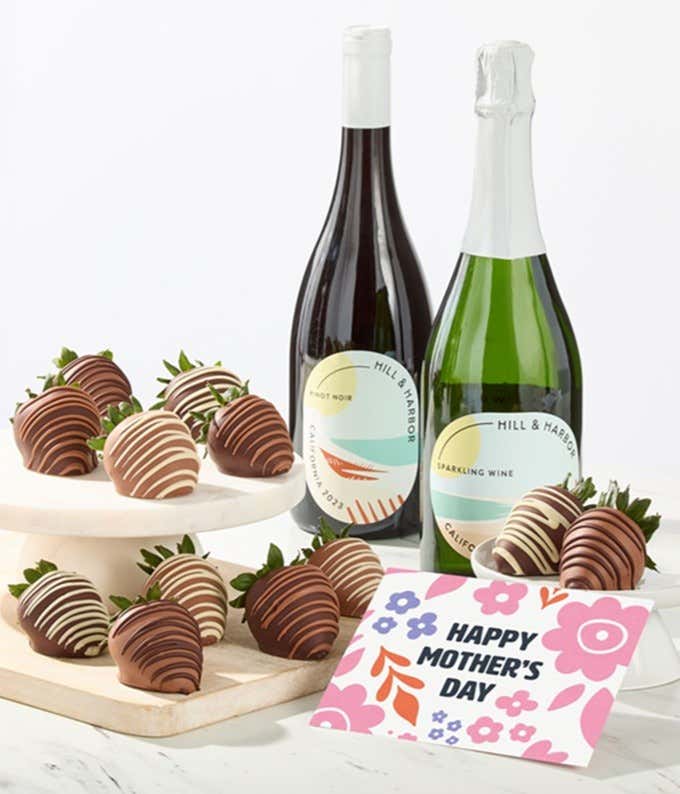Hill & Harbor Pinot Noir and sparkling wine bottles displayed with two glasses and assorted chocolate-covered strawberries on trays, styled with a floral Happy Mother’s Day card for a premium wine gift.