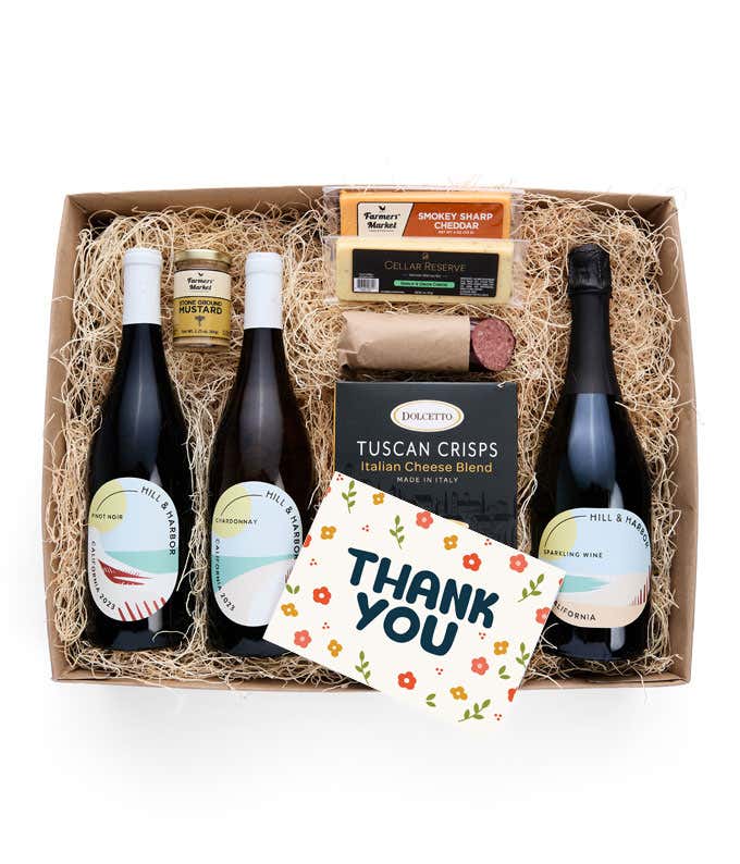 A gift box with three bottles of California wine (red, white, and sparkling), two types of cheese, crackers, stone-ground mustard, a summer sausage, and a Thank You message card.