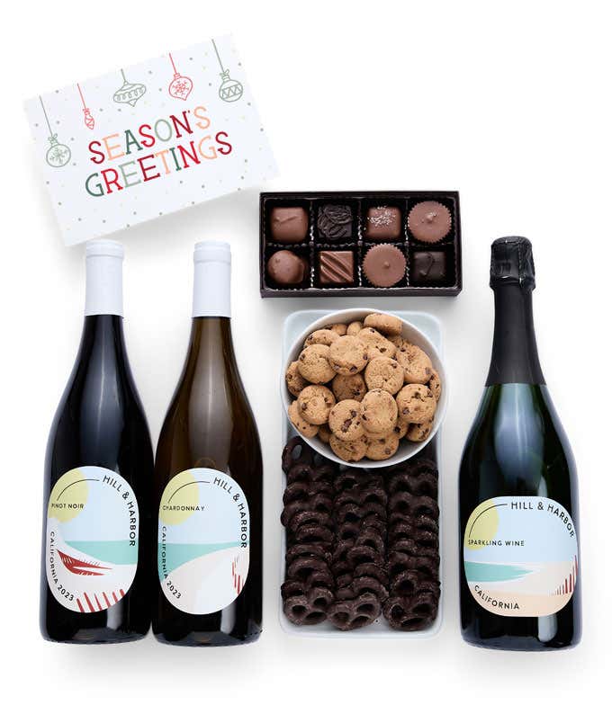 A holiday gift set with three bottles of Hill & Harbor wine (Pinot Noir, Chardonnay, and sparkling wine), a box of assorted chocolates, chocolate-covered pretzels, a box of mini chocolate chip cookies, and a Season's Greetings message card.