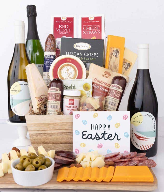 A wooden gift basket filled with summer sausages, 3 cheeses, Tuscan crisps, mini toasts, red velvet cookies, cheese straws, nuts, mustard, and 3 bottles of wine with an Easter card.