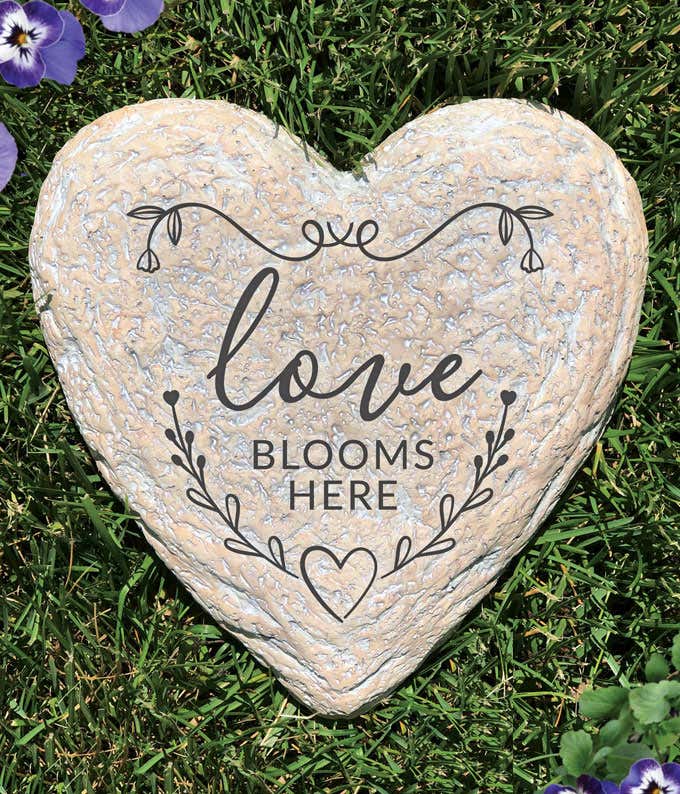 Heart shaped garden stone with the quote: love blooms here on it.