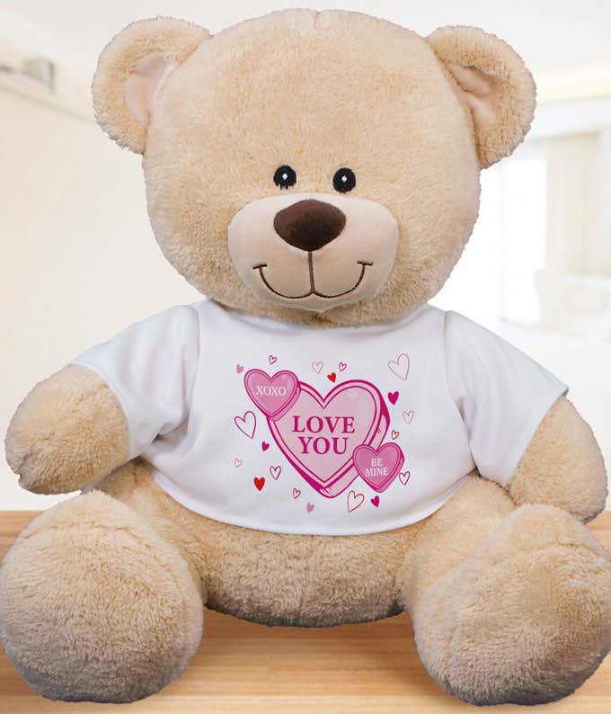 Beige stuffed teddy bear with a white t-shirt filled with conversation hearts with sayings like XOXO, Be Mine, and Love You