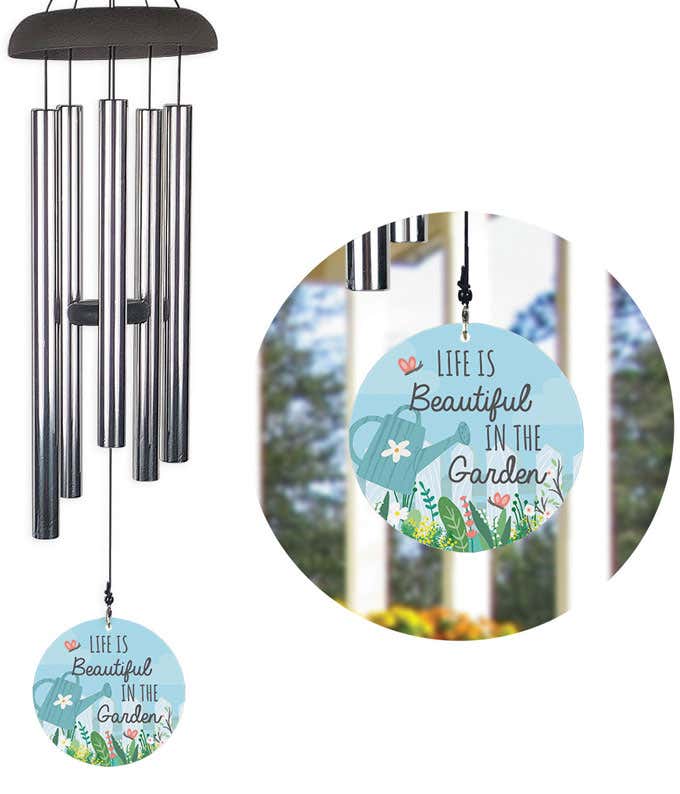 A wind chime with a white picket fence, watering can and garden motif and the quote, Life is beautiful in the garden
