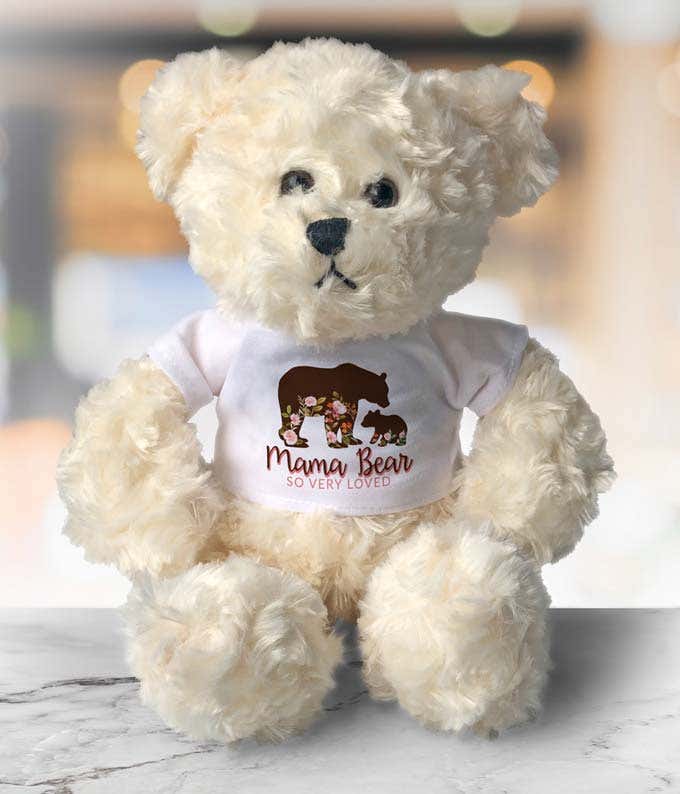 Cream-colored teddy bear with soft, fluffy fur, wearing a white shirt featuring a floral silhouette of a mama bear and cub, along with the text Mama Bear So Very Loved