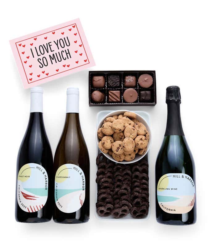 An indulgent gift set with three bottles of Hill & Harbor wine (Pinot Noir, Chardonnay, and sparkling wine), a box of assorted chocolates, chocolate-covered pretzels, a box of mini chocolate chip cookies, and a I Love You greeting card.