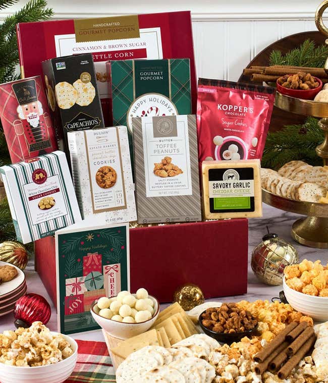  A holiday gift basket filled with assorted treats, including cinnamon and brown sugar kettle corn, peppermint wafer rolls, red velvet cookies, dipped peanuts, savory garlic cheddar cheese, Cubetti wafer cookies, gourmet popcorn, and Capeachio's crackers.