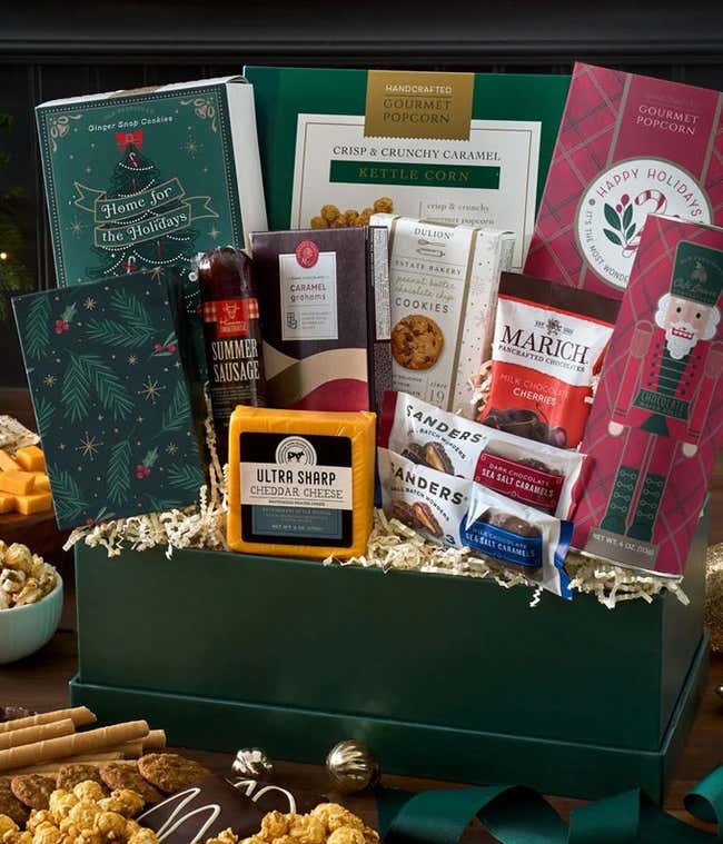 Gift basket includes assorted treats such as pretzel twists, flatbread, key lime cookies, gourmet popcorn, toffee peanuts, summer sausage, cheese, cubetti, chocolate squares, caramel popcorn, mixed nuts, pretzels, chocolate-covered wafers, and a decorativ