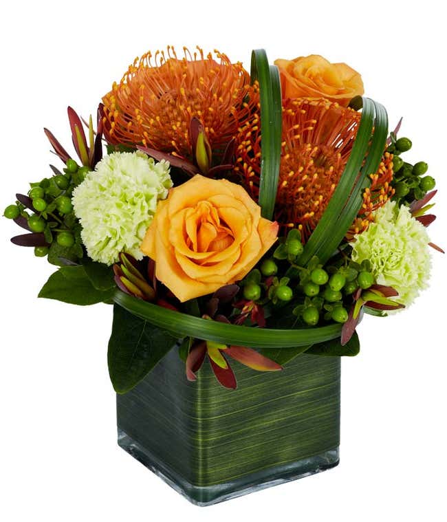 Orange roses, orange spider mums and green carnations in a modern square vase