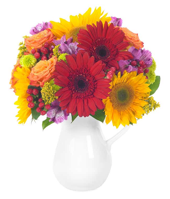Red and yellow gerbera daisies, orange roses and hypericum in reusable pitcher