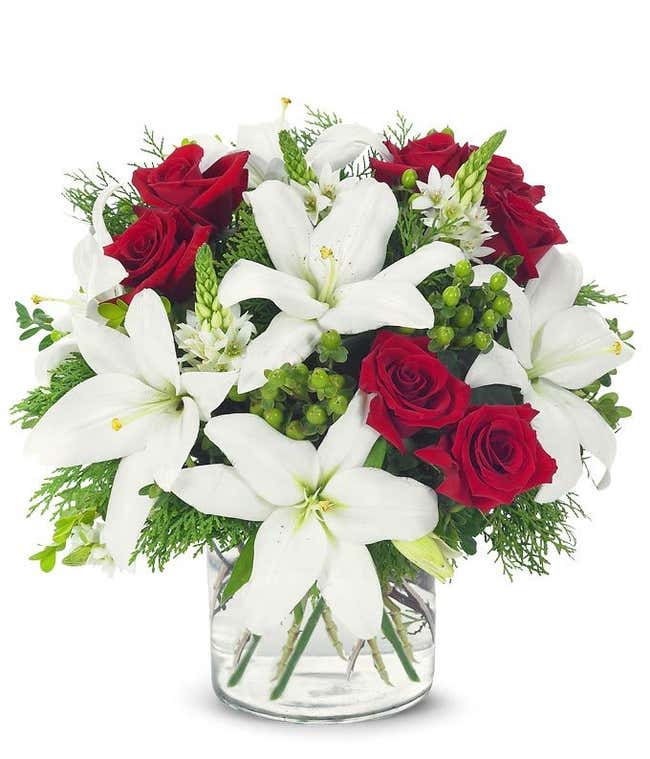 Red roses, white lilies and hypericum in circular glass vase