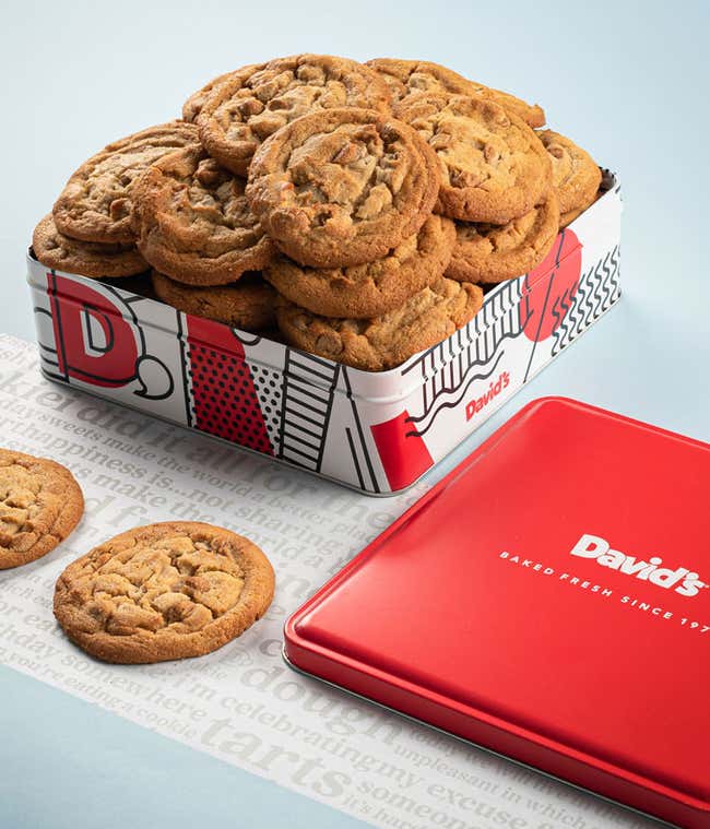 A decorative tin filled with David's cookies, primarily peanut butter flavor. The tin features a red, white, and black design with the David's logo. A few cookies and the red lid are placed beside the tin.