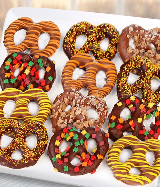 A delightful assortment of twelve pretzels dipped in milk, dark, and white chocolate, decorated with fall-themed sprinkles and candies.