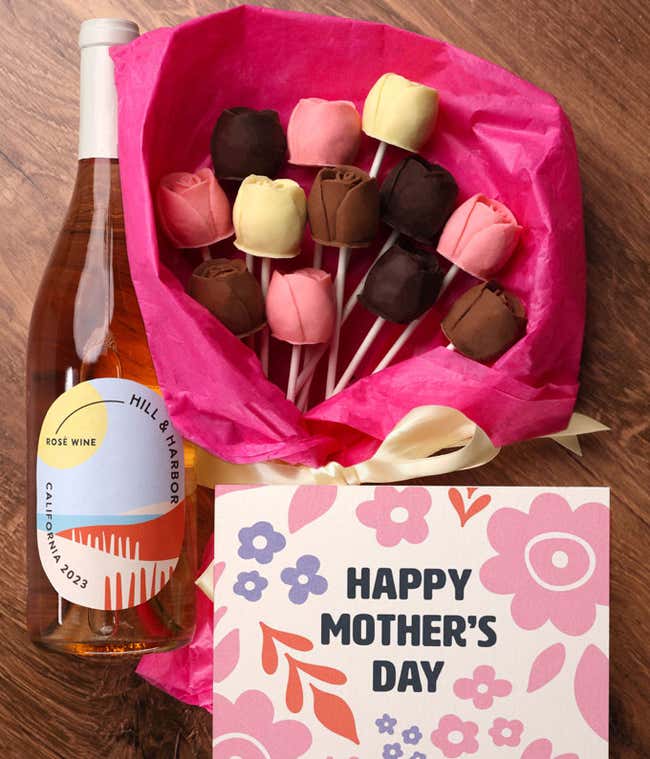A bouquet of Belgian chocolate roses in milk, dark, and white chocolate, wrapped in pink tissue paper and tied with a cream ribbon, accompanied by a bottle of ros&eacute; wine and card reading 
