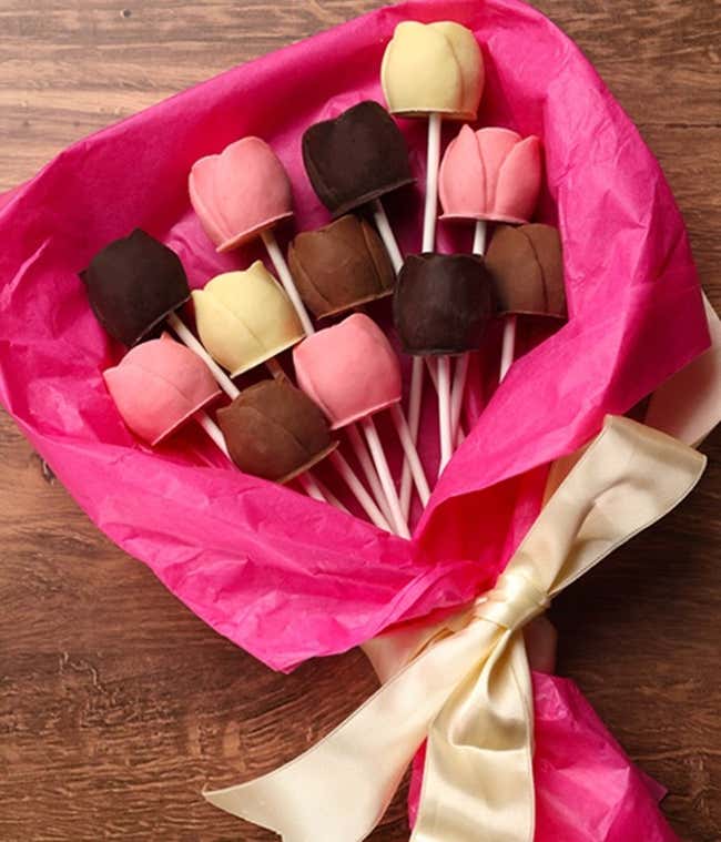 A bouquet of Belgian chocolate roses in milk, dark, and white chocolate, elegantly wrapped in pink tissue paper and tied with a cream ribbon.