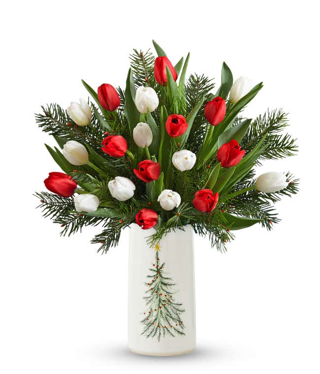 Red and white tulips with seasonal greens in a glass vase, creating a vibrant and elegant floral arrangement.
