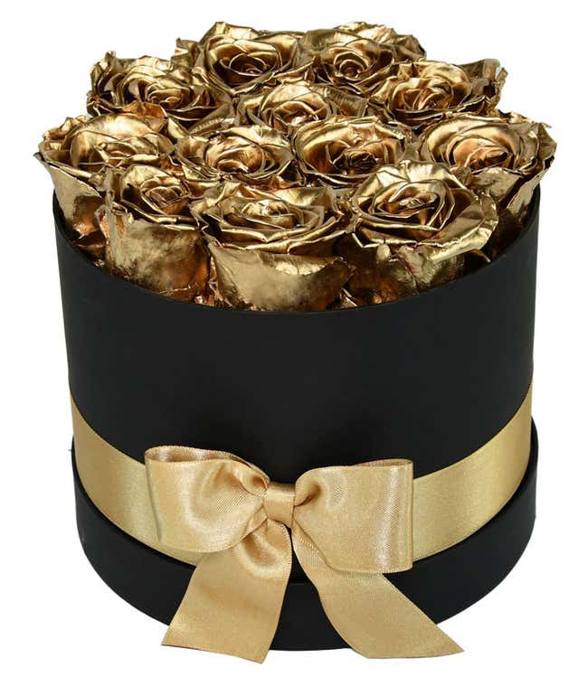 One dozen gold preserved roses arranged in a black hat box with a gold ribbon.