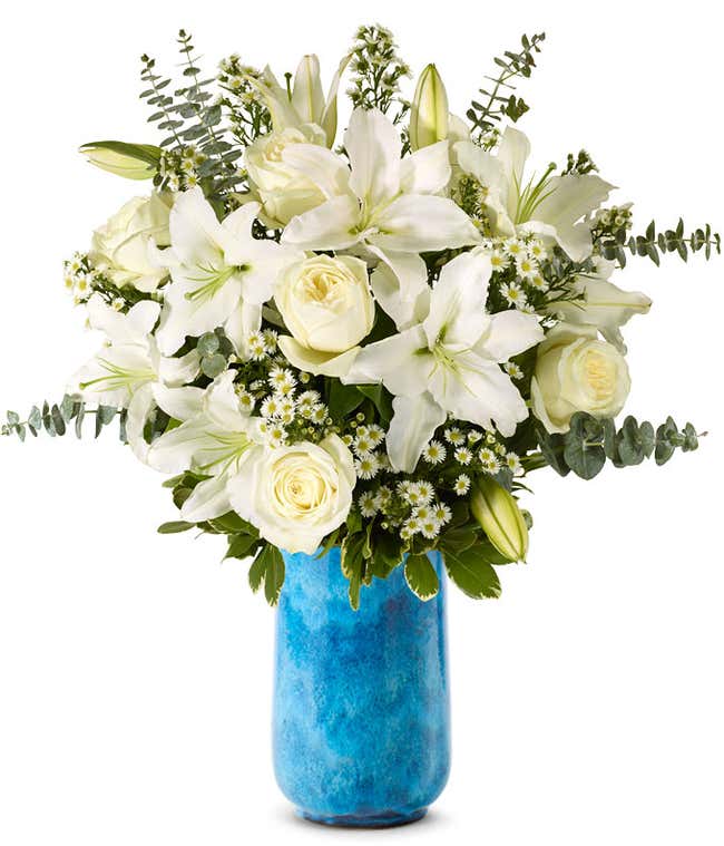 An elegant floral arrangement featuring white roses, white lilies, white asters, and eucalyptus, optionally displayed in a glass vase.