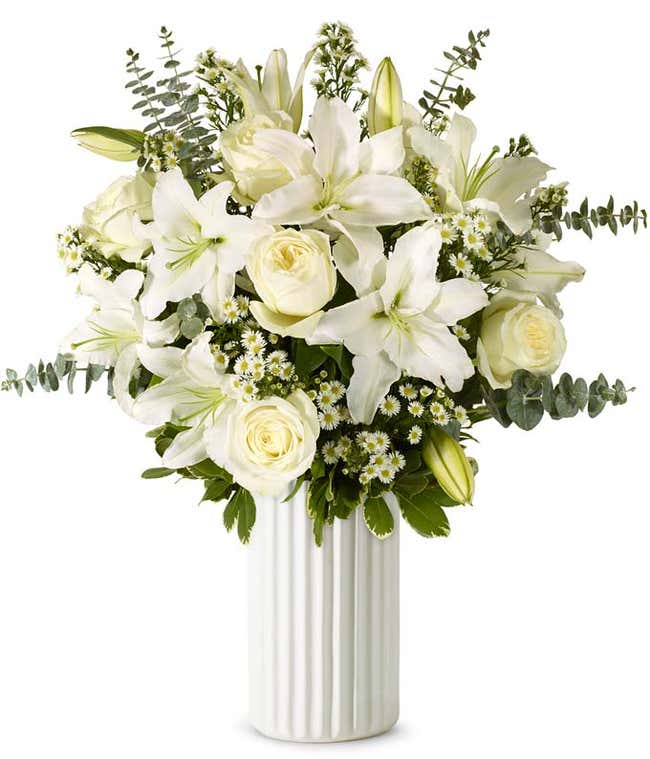 An elegant floral arrangement featuring white roses, white lilies, white asters, and eucalyptus, optionally displayed in a glass vase.