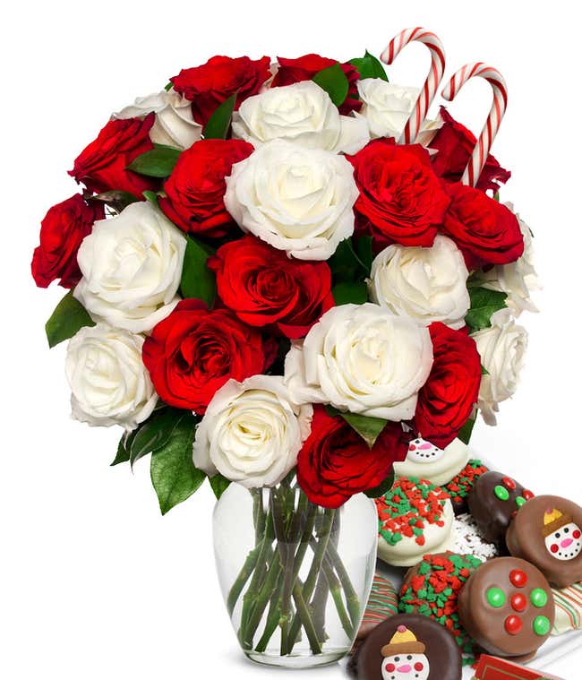 12 red and 12 white roses and 2 candy canes popping out of a glass vase with some leaves showing. Next to it is a plate of chocolate cookies with red/green sprinkles, candy, and snowmen.