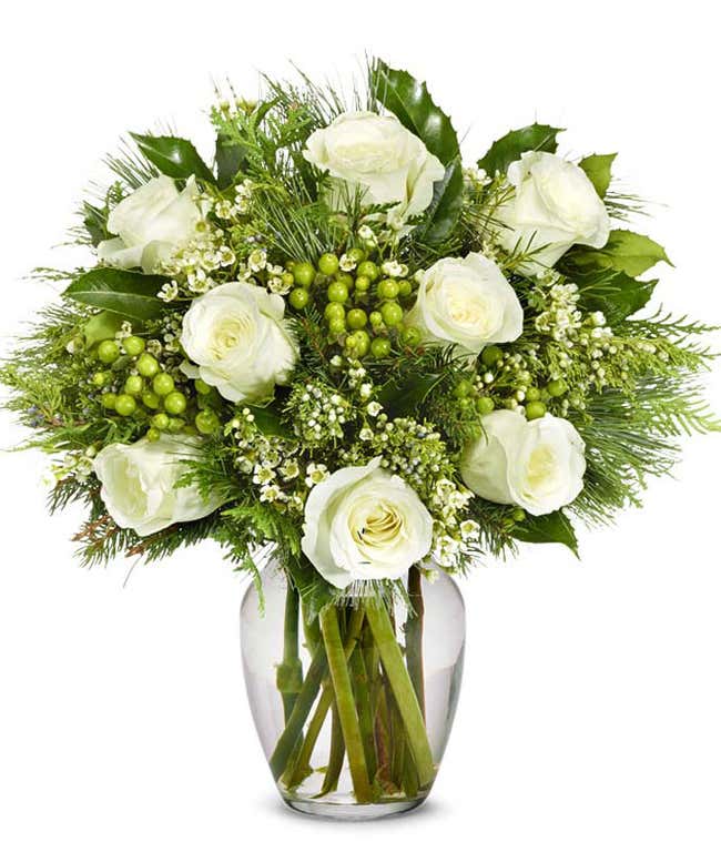 Elegant bouquet featuring white roses, green berries, and assorted greenery, arranged in a clear glass vase. The mix of lush foliage and delicate flowers creates a fresh and sophisticated display.