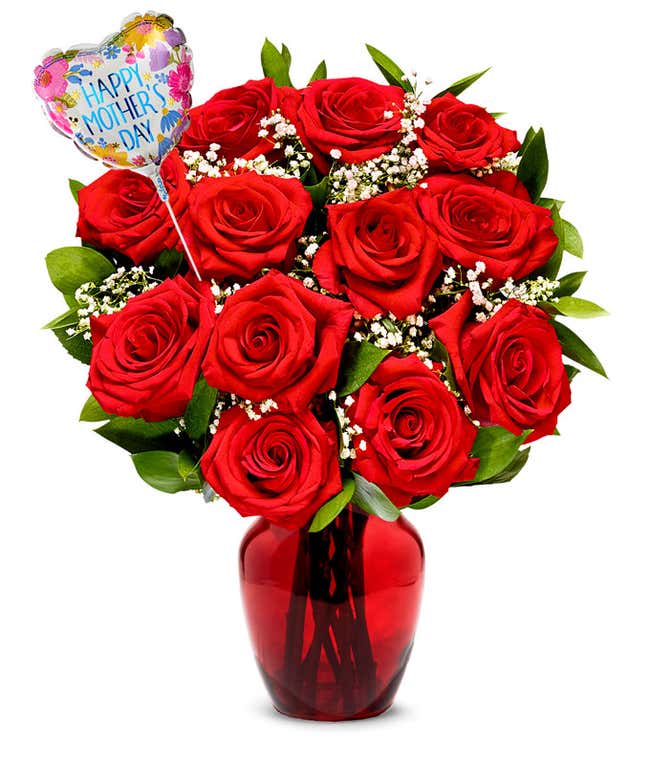 One dozen red roses with pops of greenery and white baby's breath in a clear glass vase with a pink and red heart shaped balloon reading happy mother's day
