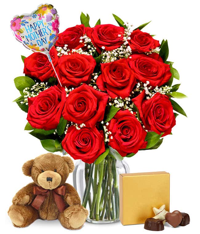 dozen red roses with greenery and baby's breath in a clear glass vase. Sat next to it is a brown teddy bear and a brown &amp; gold square box of chocolates. And a pink and red heart shaped balloon reading happy mother's day