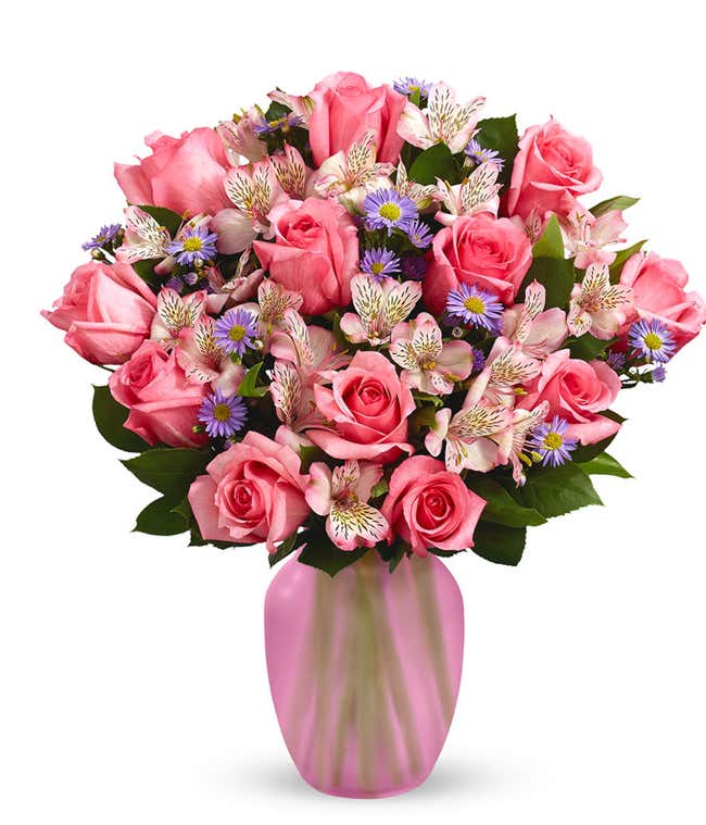 A bouquet of pink roses, white alstroemeria, and lavender aster in a glass vase 