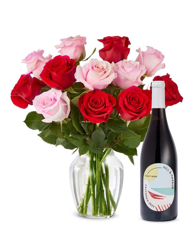 A mix bouquet of one dozen red and blush roses fills a clear glass vase and is paired with a bottle of Hill &amp; Harbor California Pinot Noir.