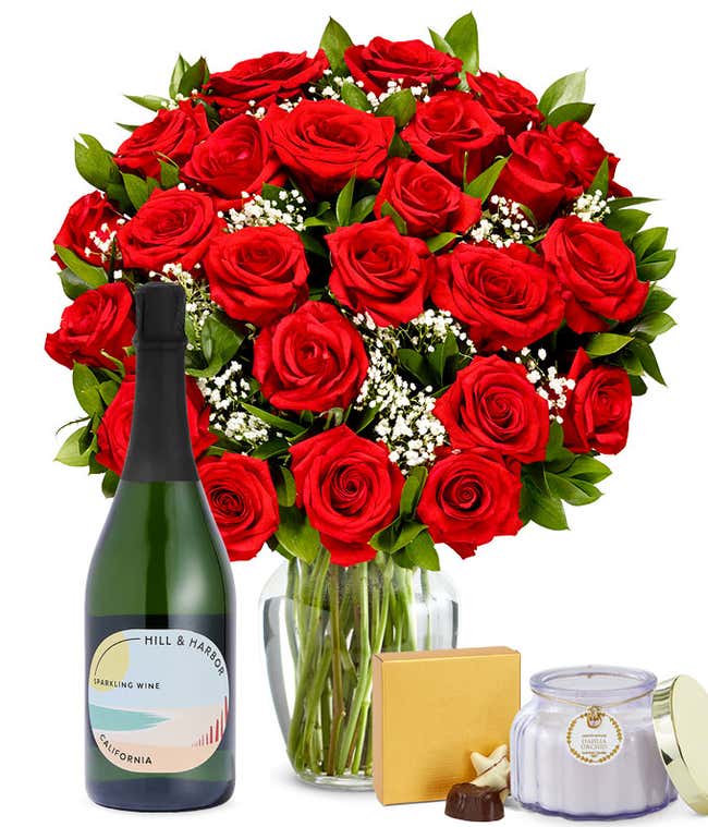 Two Dozen Red Roses in a clear glass vase with a box of chocolates, a bottle of sparkling wine, and a Dahlia &amp; Orchid scented candle
