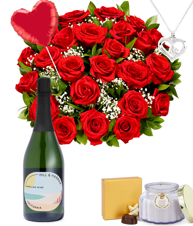 Partial image of Two Dozen Red Roses in a clear glass vase with a box of chocolates, a silver heart necklace, red heart mylar balloon, a bottle of sparkling wine, and a dahlia &amp; orchid scented candle without vase.