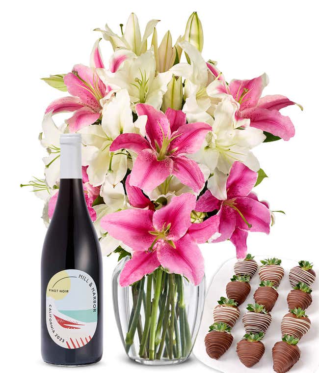 A bouquet of pink and white lilies arranged in a clear glass vase is paired with a bottle of Hill &amp; Harbor Pinot Noir and 12 chocolate-covered strawberries.