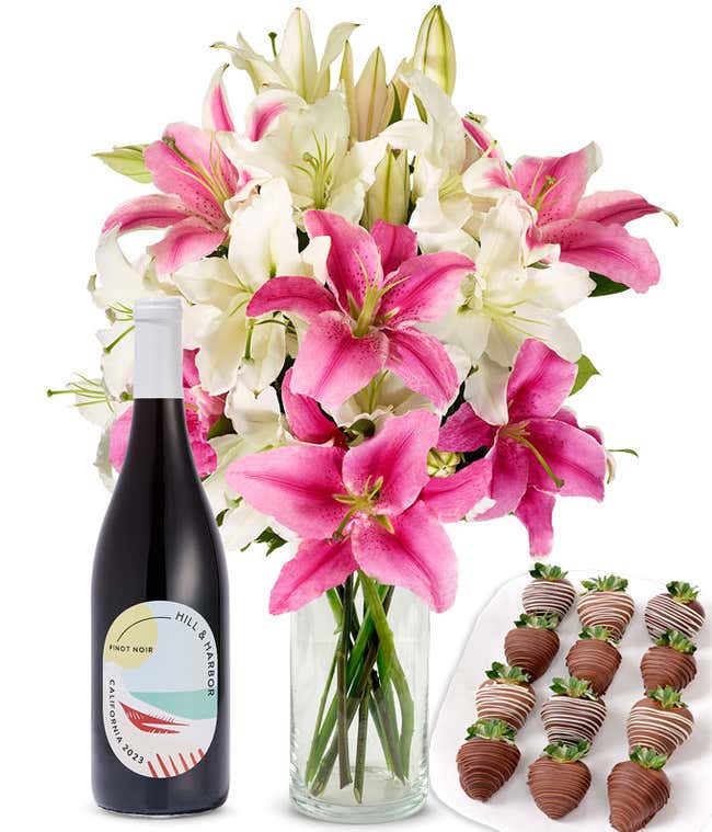 A bouquet of pink and white lilies arranged in a clear glass vase is paired with a bottle of Hill &amp; Harbor Pinot Noir and 12 chocolate-covered strawberries.