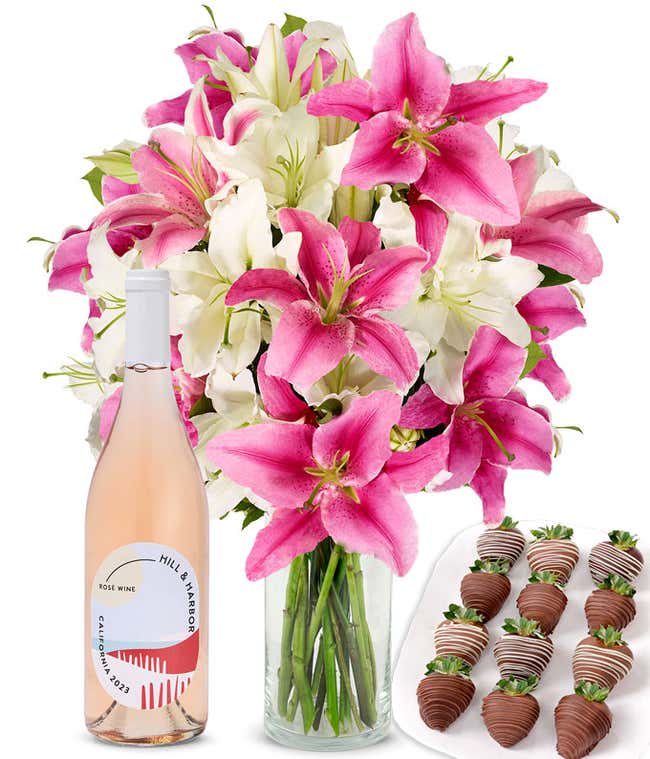 A bouquet of pink and white lilies arranged in a clear glass vase is paired with a bottle of Hill &amp; Harbor Ros&eacute; and 12 chocolate-covered strawberries.