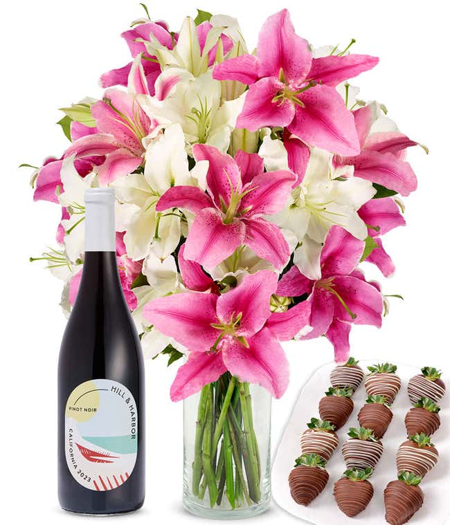 A bouquet of pink and white lilies arranged in a clear glass vase is paired with a bottle of Hill &amp; Harbor Pinot Noir and 12 chocolate-covered strawberries.