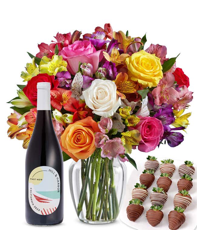 A bouquet of colorful roses and alstroemeria in a clear vase is displayed beside a bottle of Hill &amp; Harbor Pinot Noir and 12 chocolate-covered strawberries.