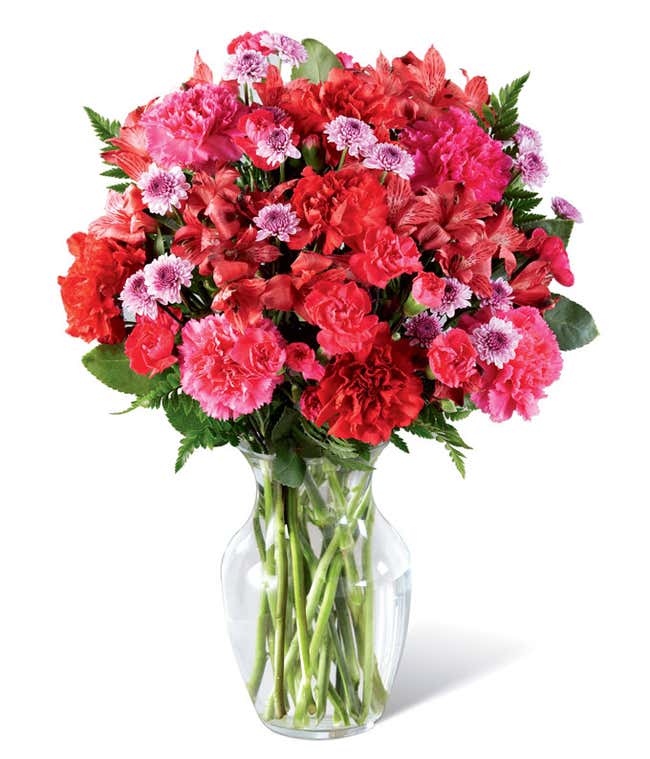 Round, full, bouquet of red and hot pink flowers, in a clear vase