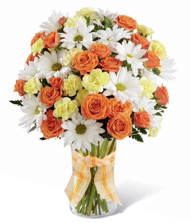 Tall and round arrangement of white daisies, yellow carns, and yellow roses in a cylinder vase