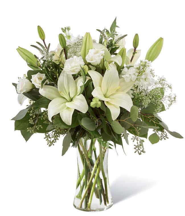 White lilies and roses, with mixed floral greens, arranged into a tall clear cylinder vase