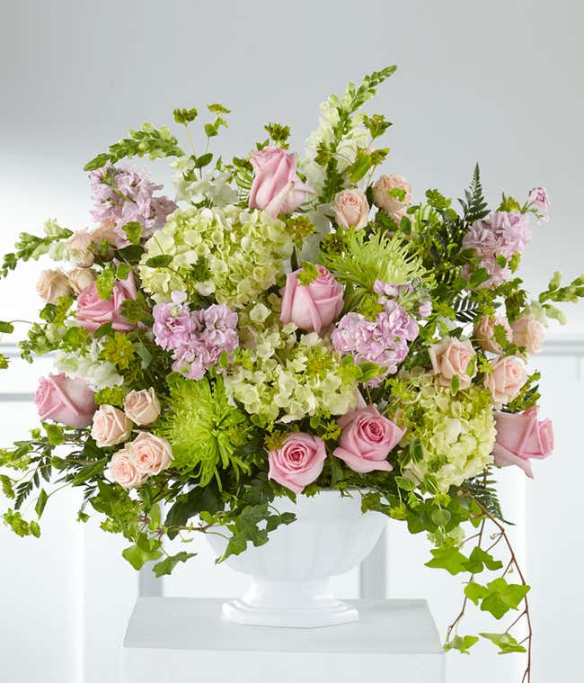 Standing basket of green hydrangeas, pink roses, and white snapdragons, in a white plastic urn