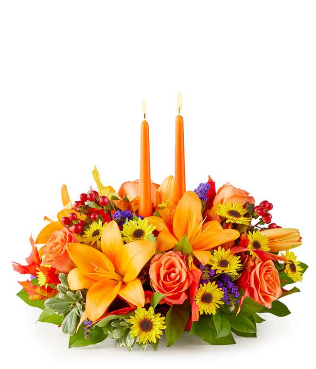 Fall centerpiece with orange candles, orange lilies, roses, yellow poms, purple statice, and red hypericum berries.