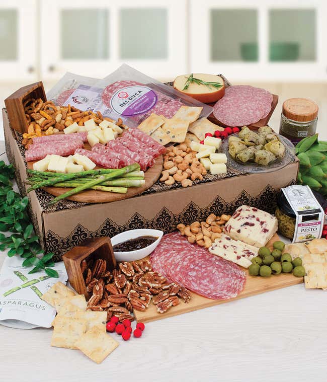 Charcuterie gift box with assorted salami, cheeses, crackers, olives, nuts, asparagus, artichokes, fig spread, and pesto arranged on a wooden board and decorative box.
